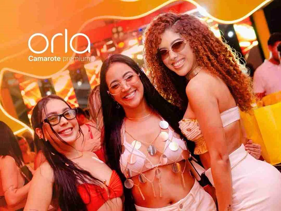 Três pessoas posam em uma ativação do Camarote Orla.