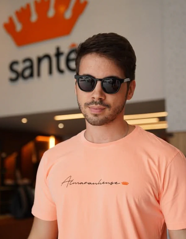 Homem com óculos escuros e camiseta salmão em frente à loja Santê.