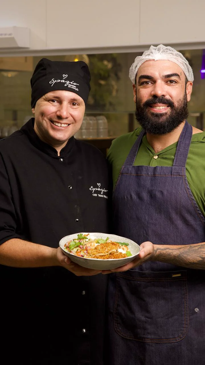 Dois profissionais de cozinha posam segurando um prato.