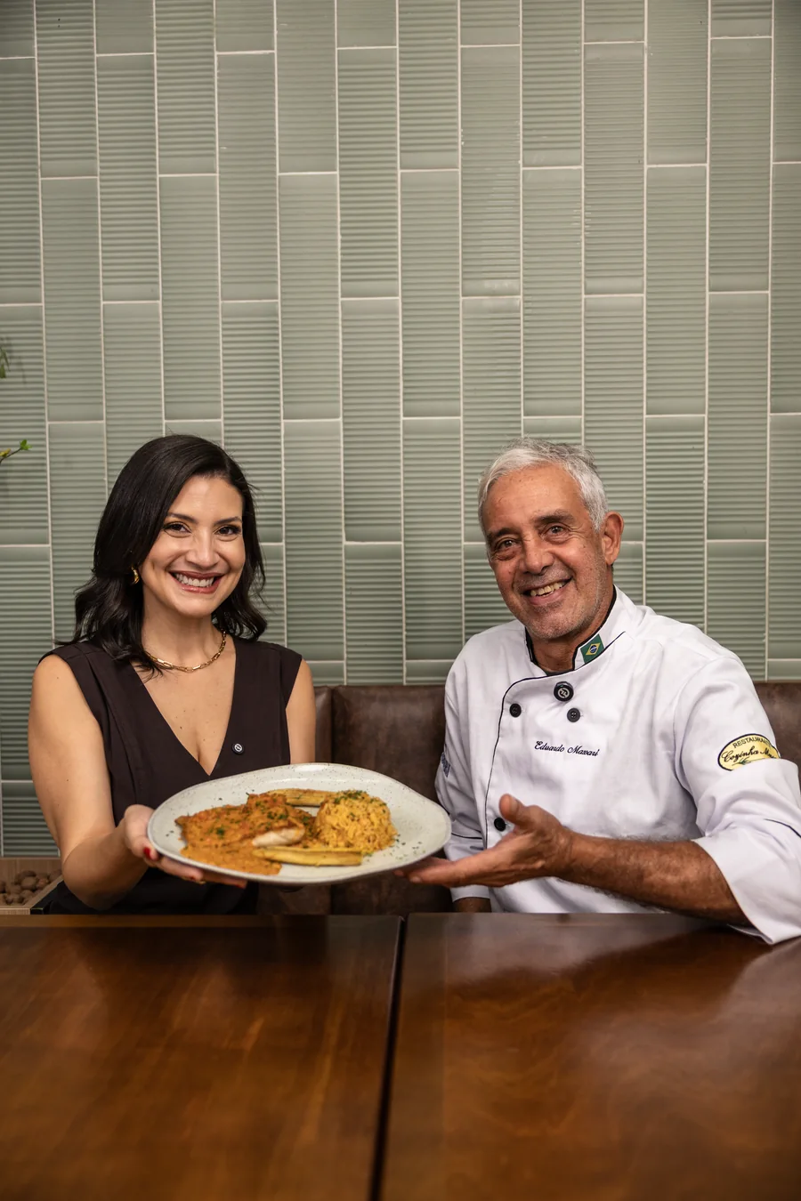 Mulher e chef sorriem enquanto apresentam um prato.